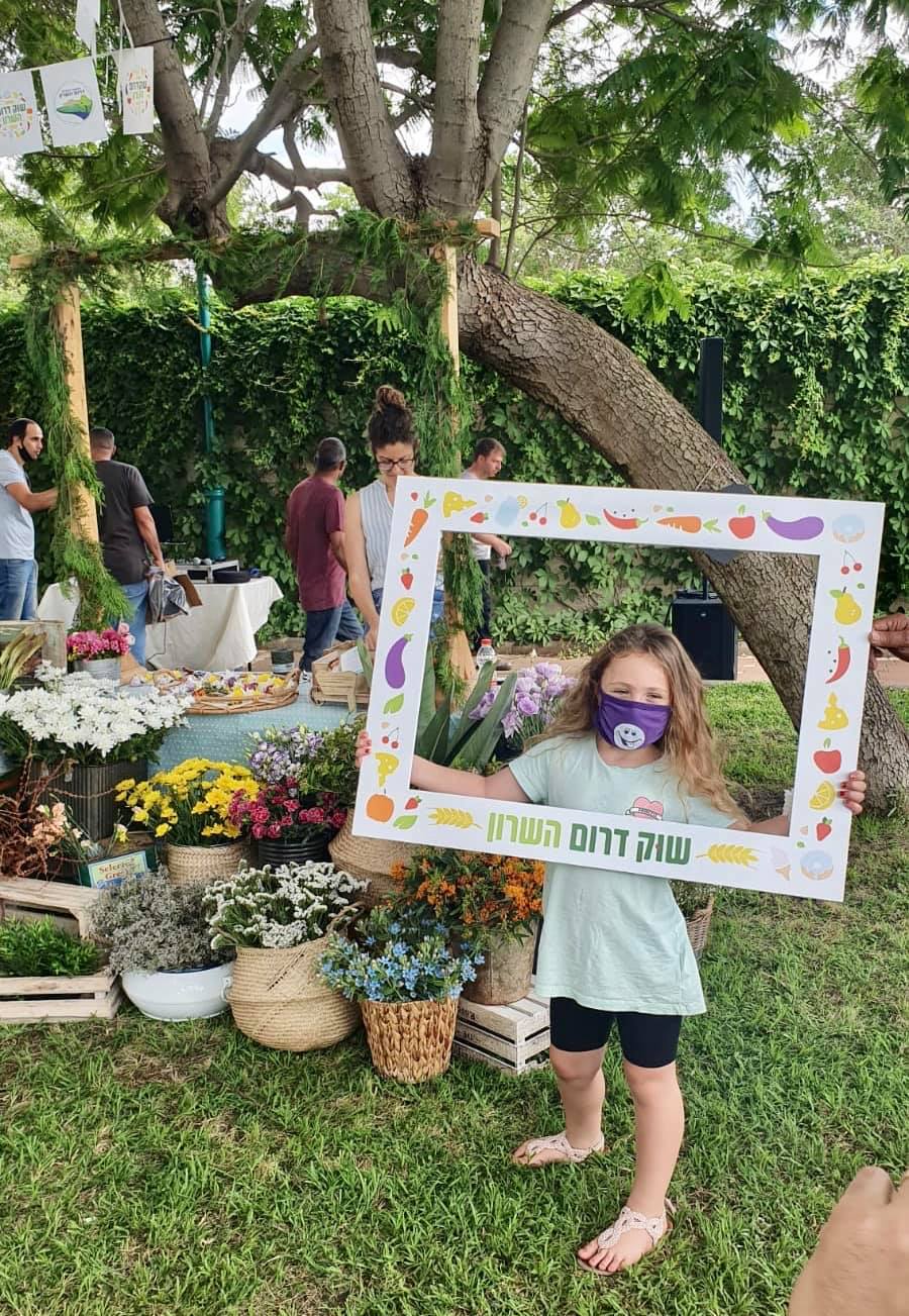 ילדה עם מסכה מחזיקה את שלט שוק דרום השרון